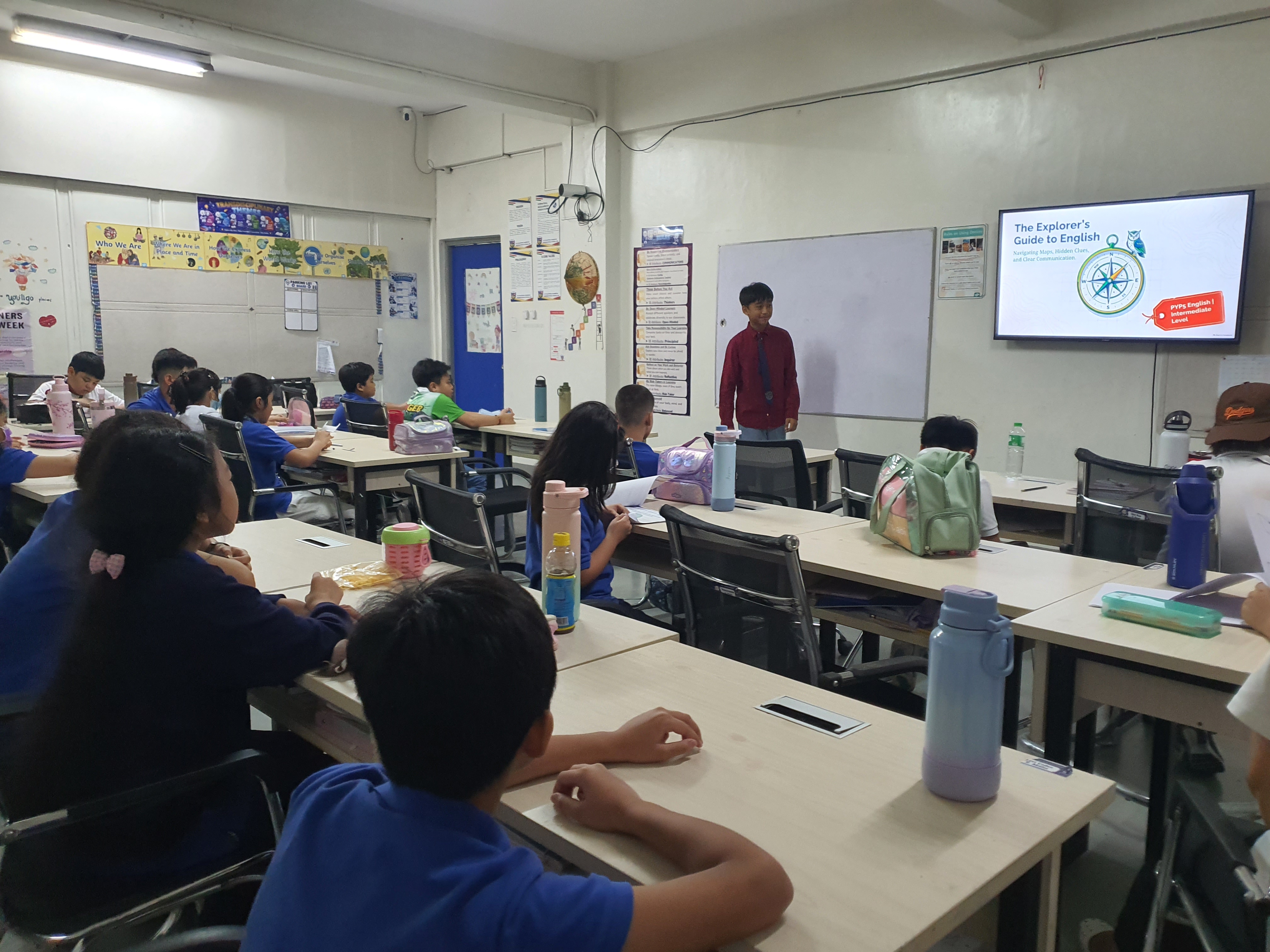 A PCIS student presenting an English lesson titled “The Explorer’s Guide to English” to classmates during the Teacher-for-a-Day activity, demonstrating the responsibility of guiding younger learners through classroom instruction.