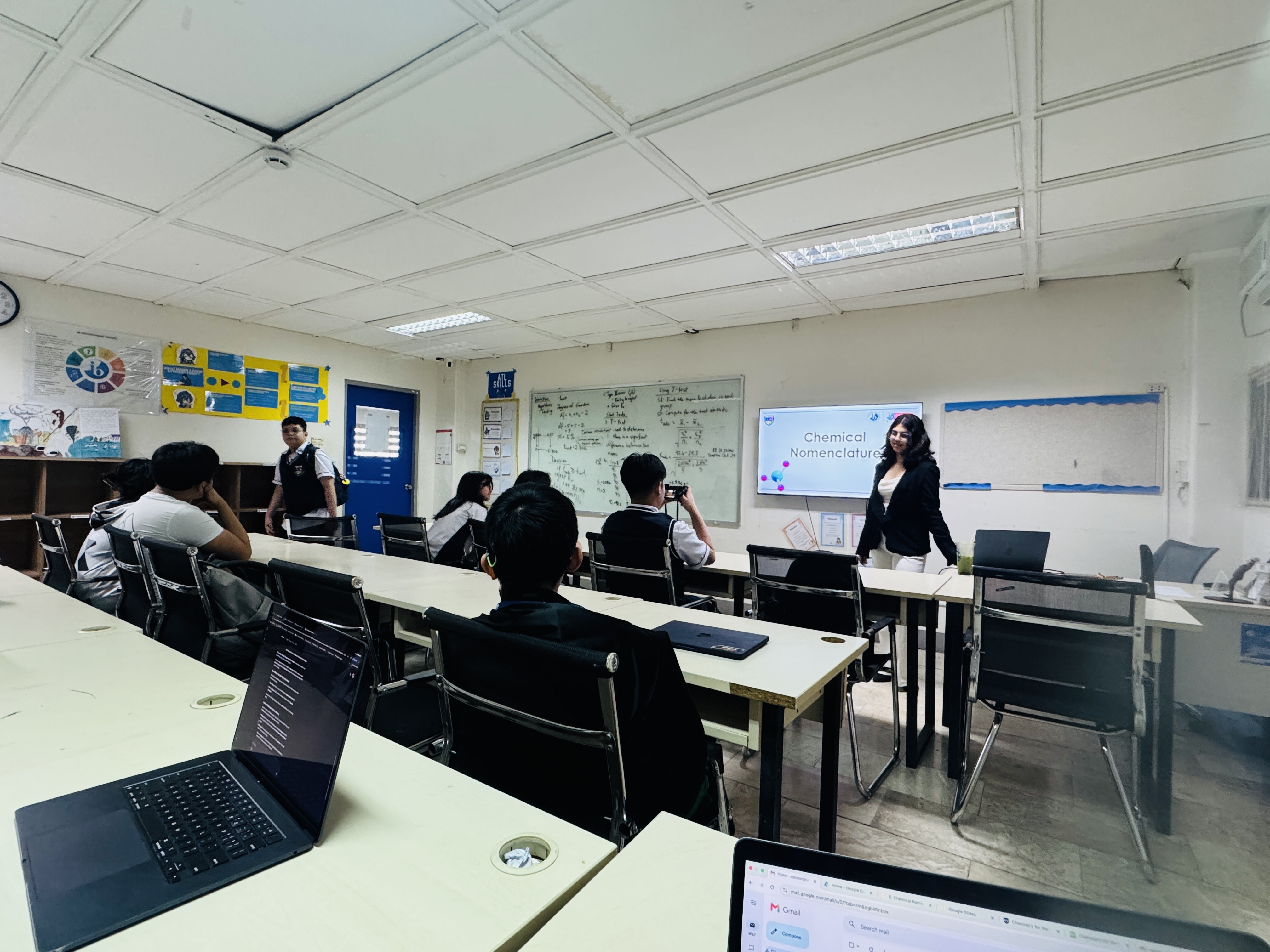 A PCIS student explaining chemical nomenclature to classmates using a classroom presentation during the Teacher-for-a-Day activity, giving learners an opportunity to experience teaching and share their understanding of a subject.